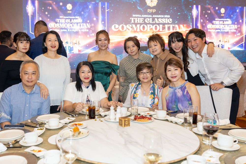 A group of people pose together at a formal dinner event with Cosmopolitan signage and blue lighting in the background.