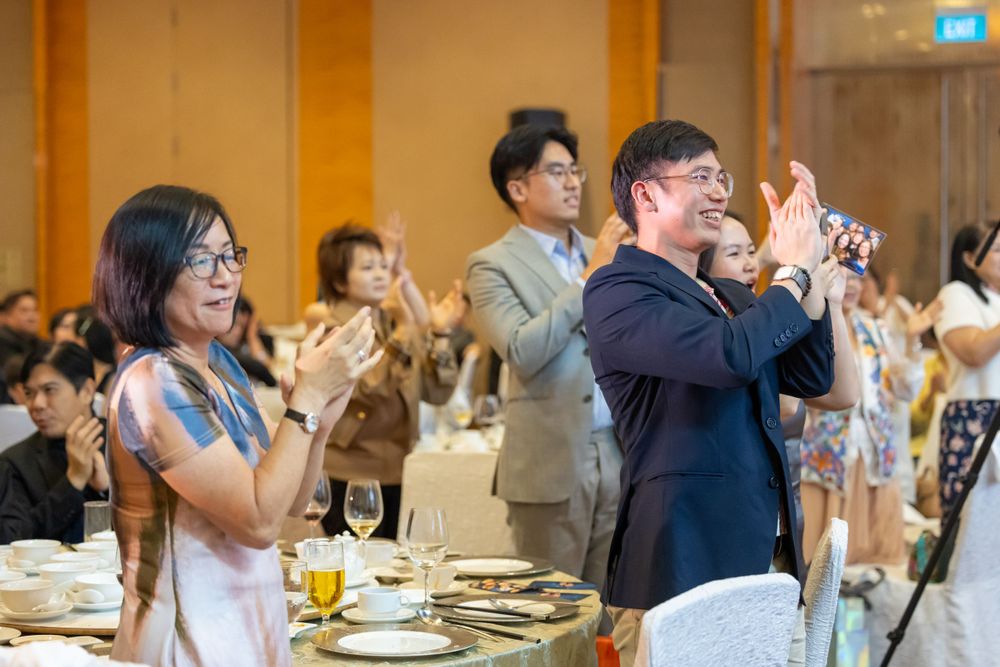 Wedding guests standing at tables and clapping during a celebration in a banquet hall.