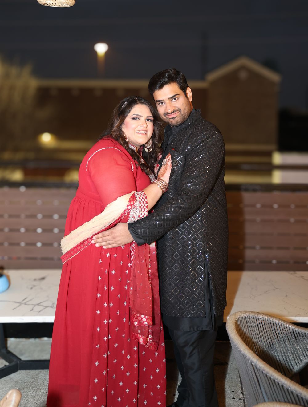 Couple in formal attire sharing a romantic moment outdoors under evening lights.