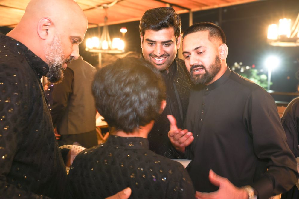 A group of men in dark formal attire having an animated conversation at an evening event.
