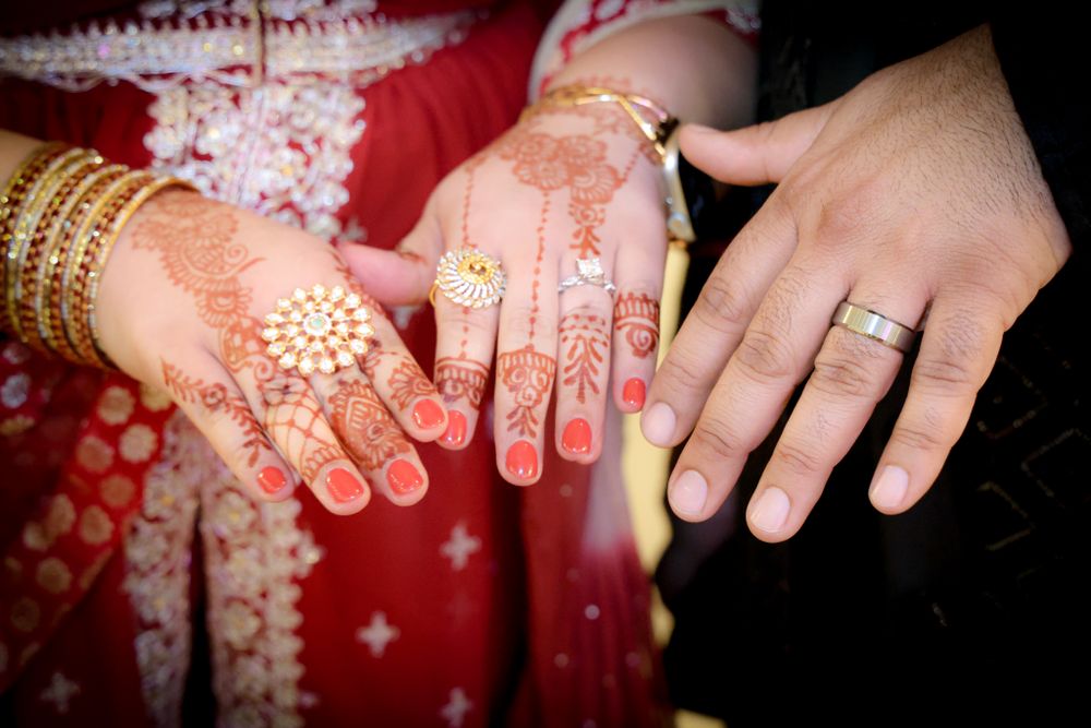 Detailed view of hands decorated with mehndi patterns and gold jewelry against a red background.