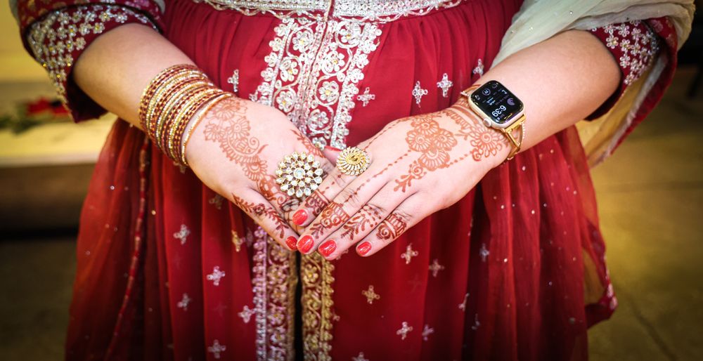 Hands adorned with henna and bangles wearing a red and gold embroidered dress.