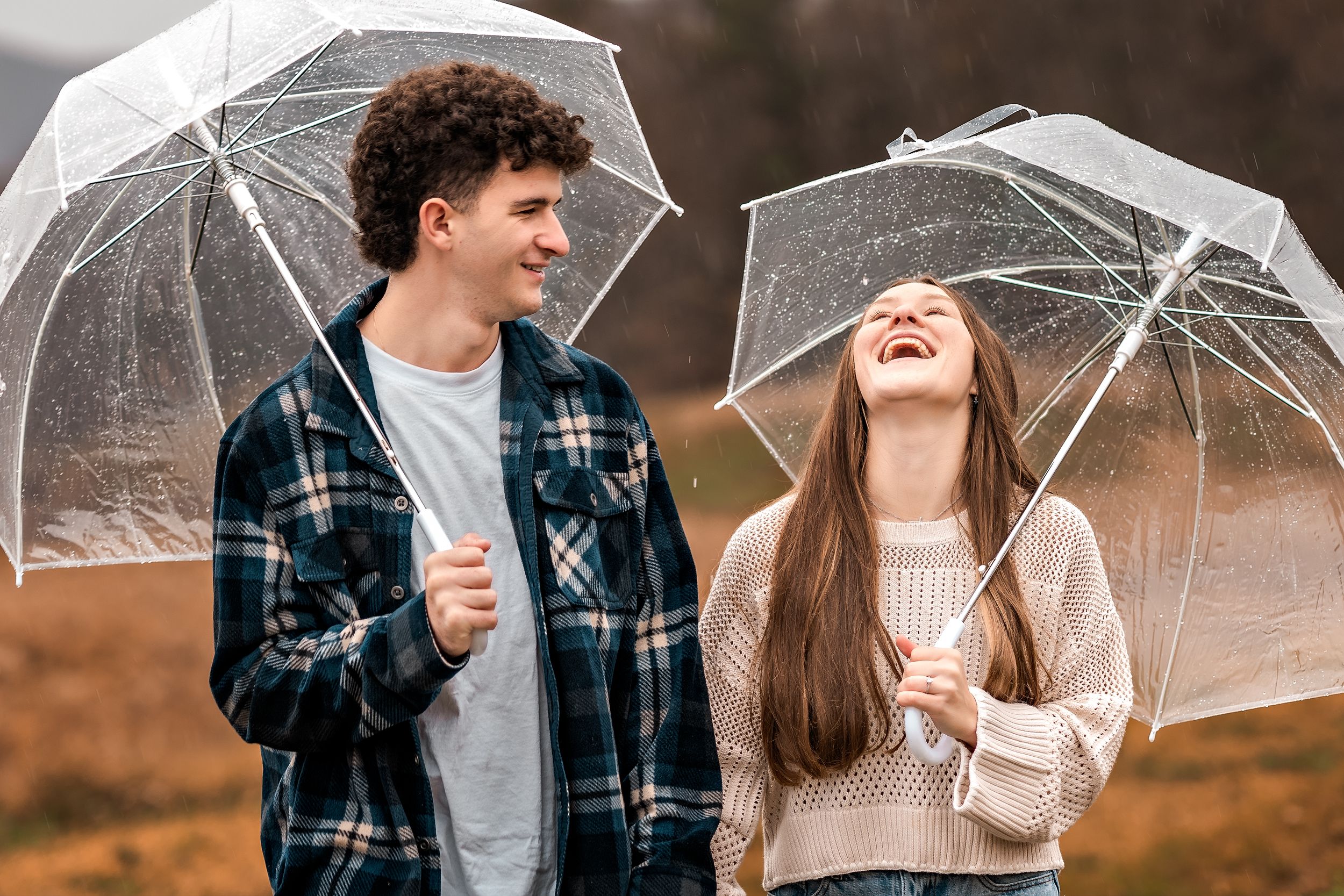 A couple shares a joyful moment together holding clear umbrellas and laughing in autumn weather.