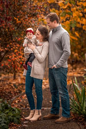 A family enjoys an autumn moment together outdoors surrounded by vibrant orange and red fall foliage.