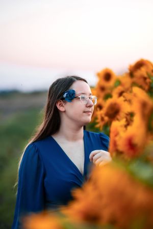 Beautiful evening scene with a person in a blue dress standing thoughtfully among vibrant orange sunflowers at sunset.