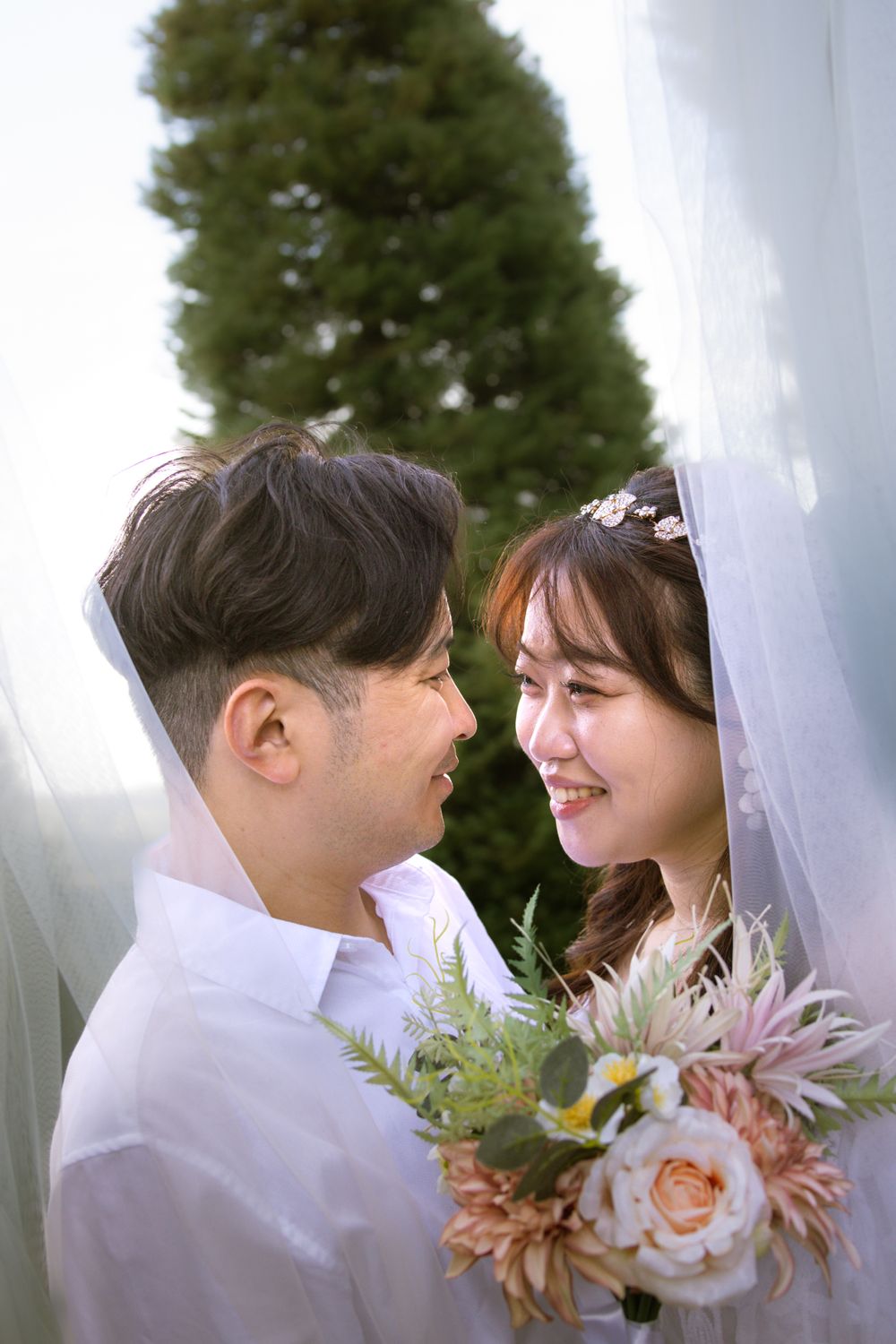 A romantic wedding portrait with couple smiling at each other and holding a floral bouquet.