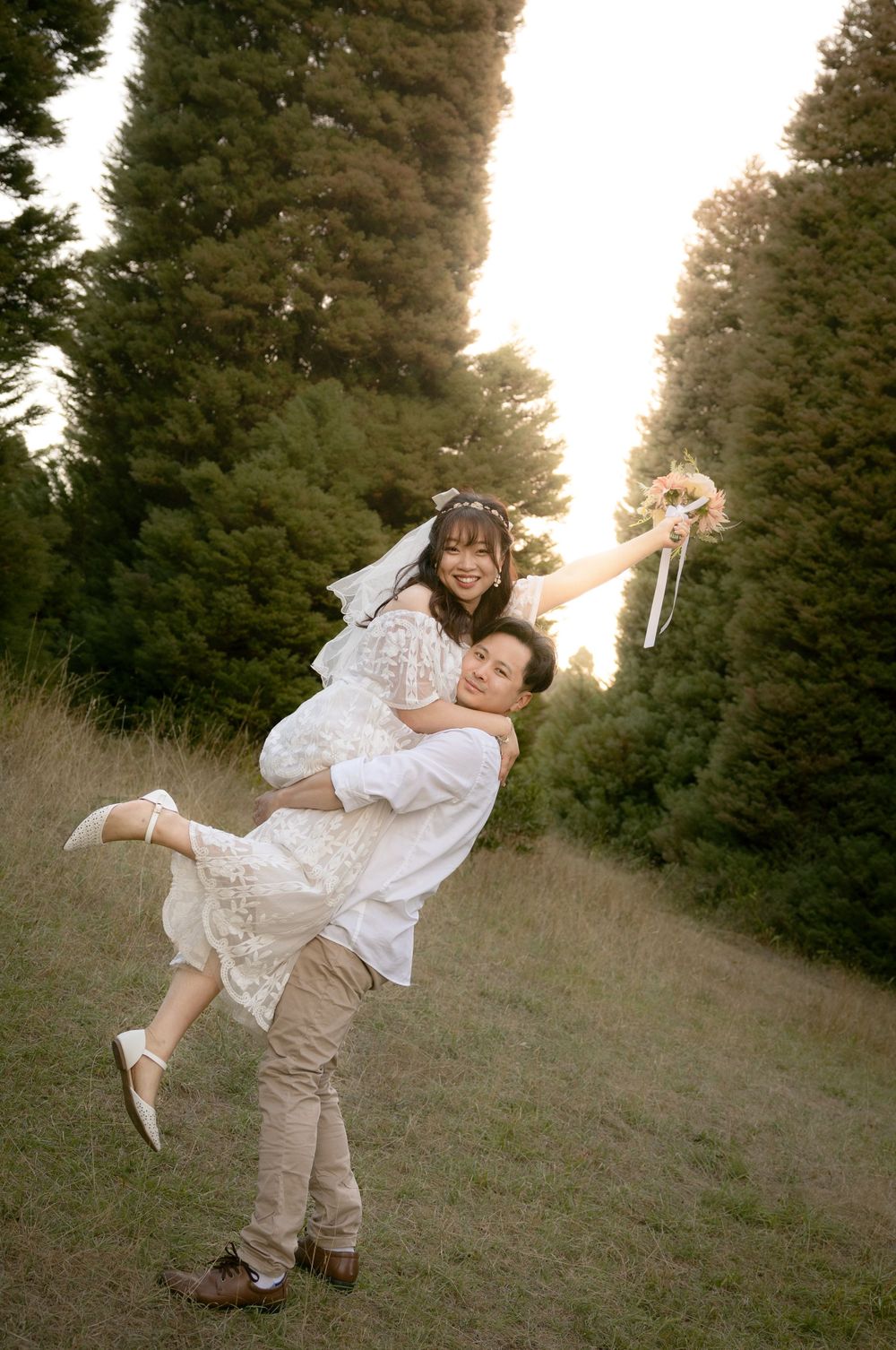 A couple performs a romantic dance lift in a mountain meadow surrounded by evergreen trees.