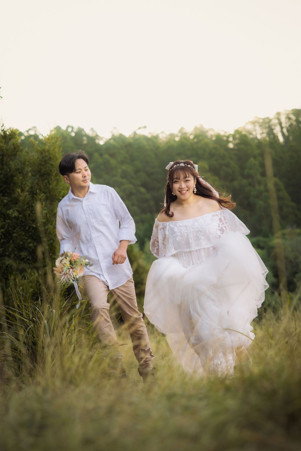 A couple runs playfully through a grassy meadow during their romantic photoshoot.