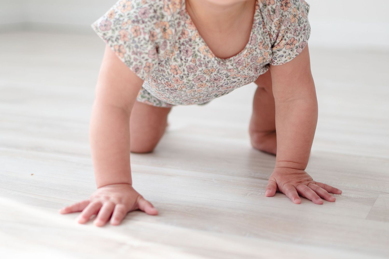Baby crawling on hardwood floor wearing a floral cotton dress.