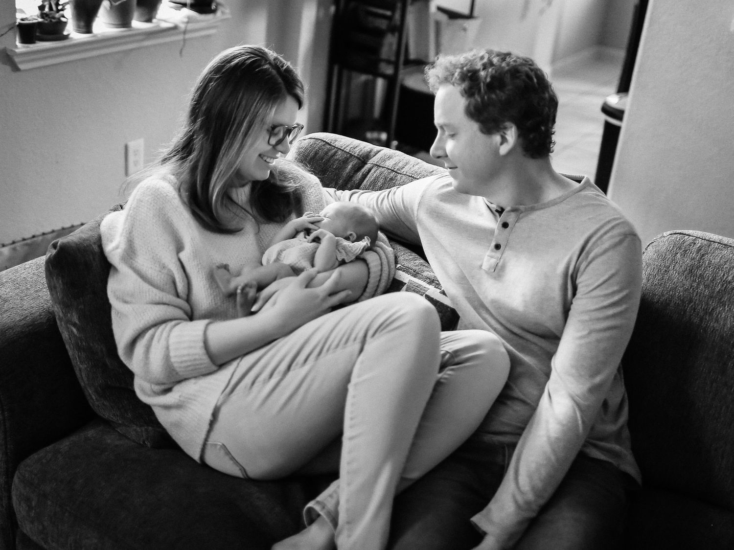 Mom, daddy and newborn baby girl snuggling on couch for In-home lifestyle session
