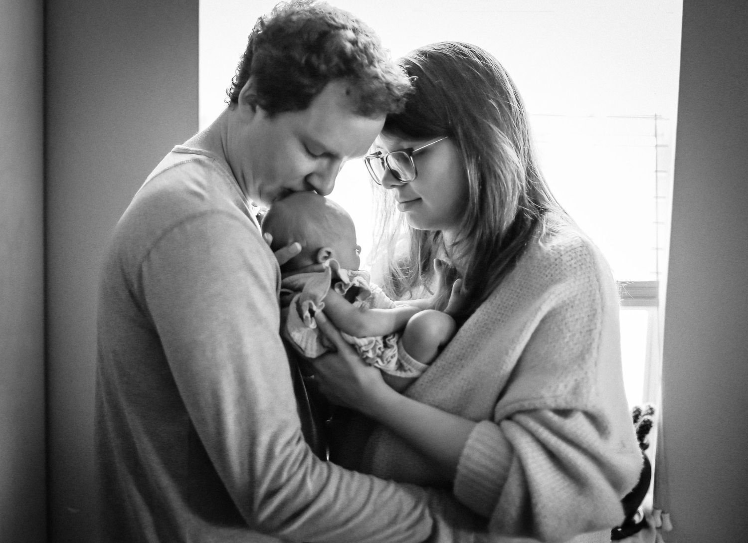 In-home lifestyle session with mom, daddy kissing babies head and daughter