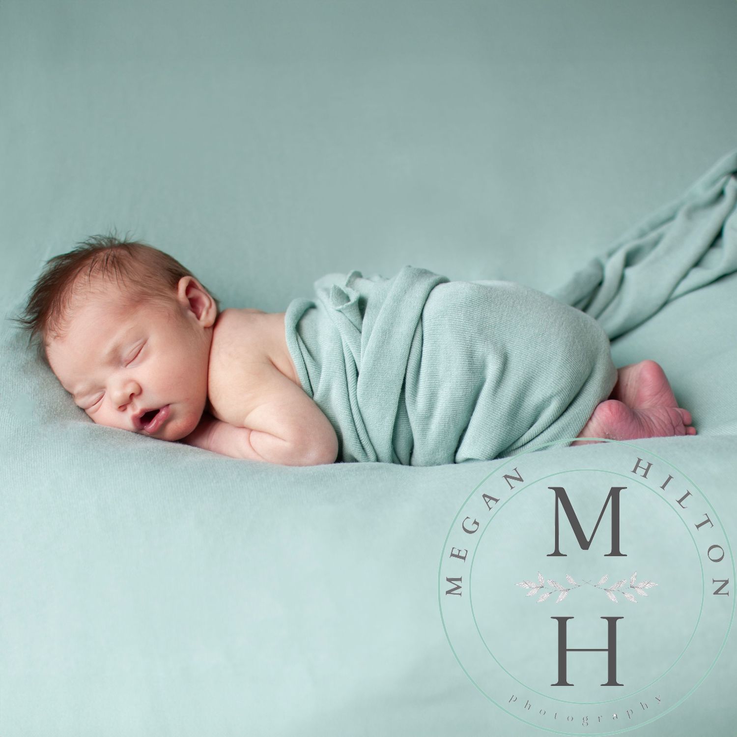 Full body image of a sleeping newborn baby swaddled in soft mint green fabric on matching background.
