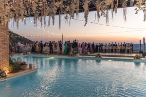 Sunset pool party with wedding guests gathered around illuminated swimming pool.