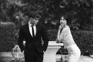 Vintage black and white photo of a couple in formal attire standing by a decorative pillar in a garden setting. Next day wedding photography