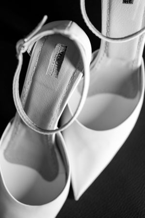 Elegant white bridal shoes with ankle straps displayed against a dark background.