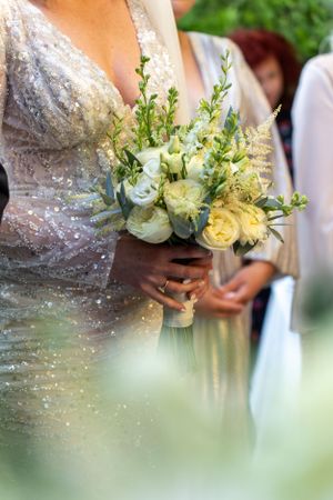 Delicate wedding bouquet with white and yellow roses held against a sequined dress.