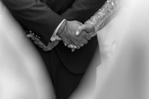 Close-up black and white shot of a couple holding hands during a wedding ceremony.