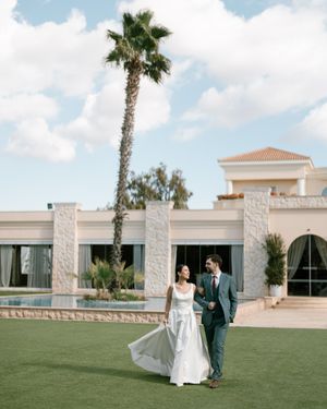 Newlyweds walking on grass with palm tree and Mediterranean style villa in background. Next day wedding photography.