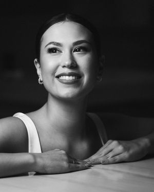 Black and white portrait of a smiling woman in a white top leaning on a table.