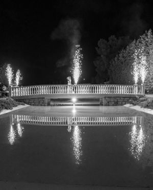 Black and white photo of illuminated fountain with fireworks reflecting in water on a wedding in Greece.