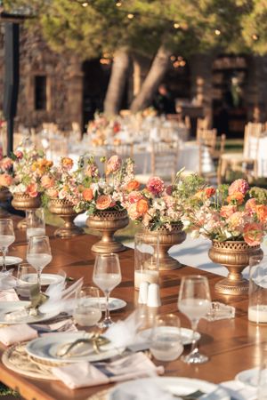 Elegant wedding table setting with gold vases filled with peach and pink floral arrangements.