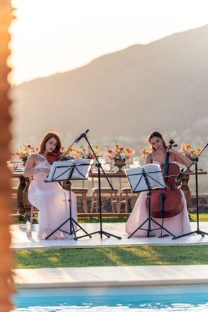 Two musicians performing with string instruments by a pool during sunset.