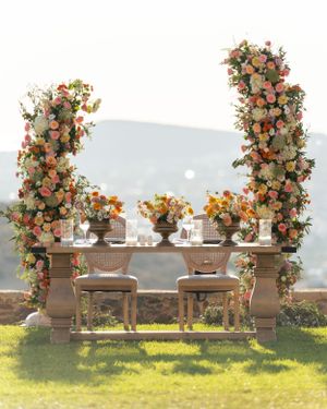 Luxurious outdoor sweetheart table with floral arch columns and mountain backdrop.