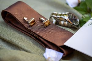 Brown necktie with golden cufflinks arranged on a textured surface.