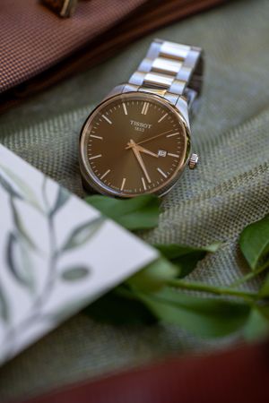 Classic Tissot watch with metal band displayed on textured fabric with greenery.