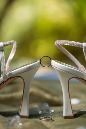 Creative wedding ring photo between two white bridal shoes with rhinestone straps.