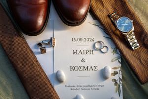 Wedding invitation with rings, dress shoes and watch arranged artistically.