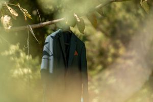 Navy blue groom's suit jacket photographed through soft-focus foliage.
