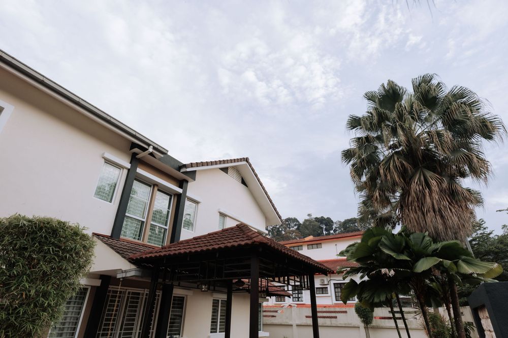 White residential house with Spanish-style architecture and a palm tree under cloudy skies.