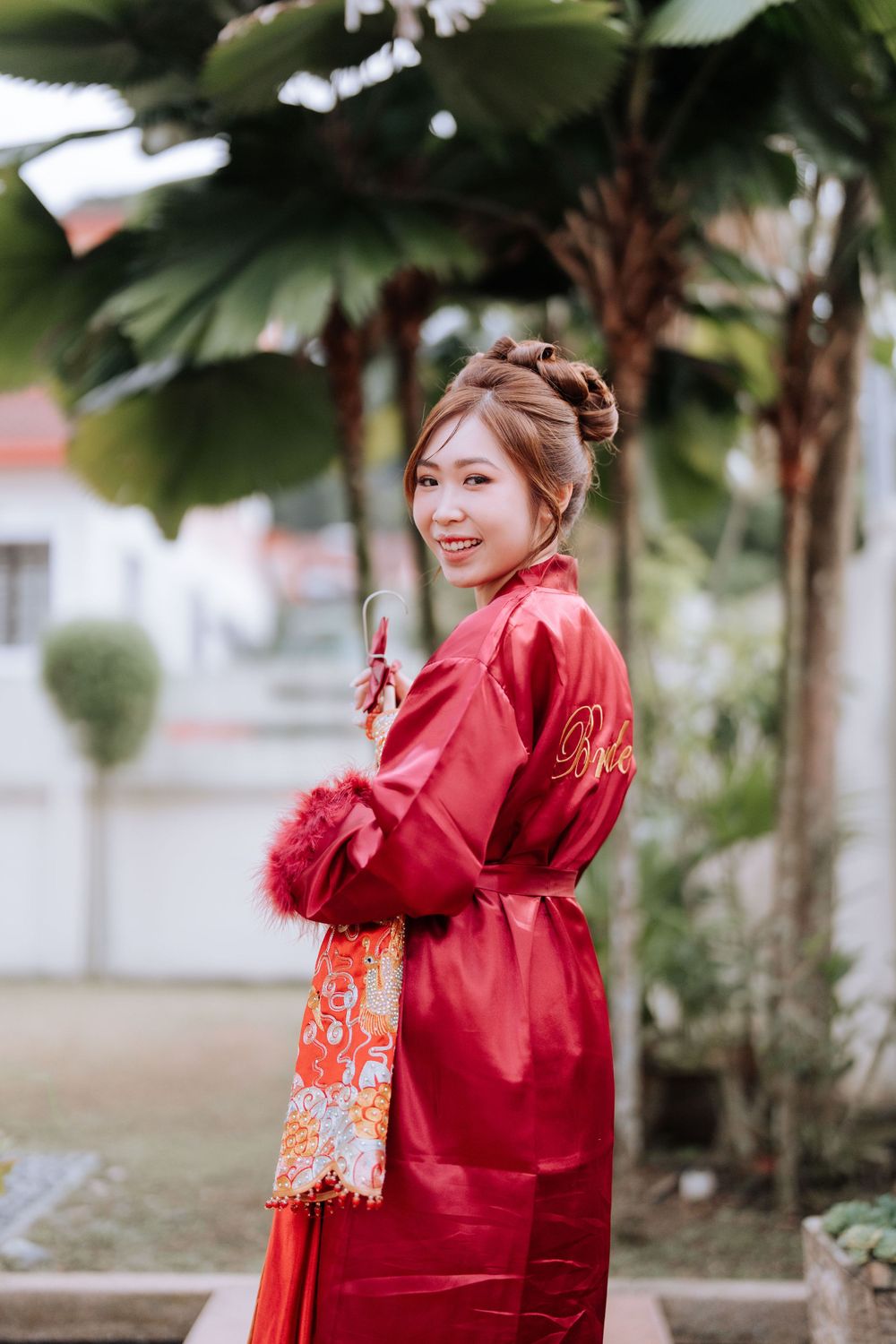 Person wearing red silk robe posing in garden setting with palm trees.