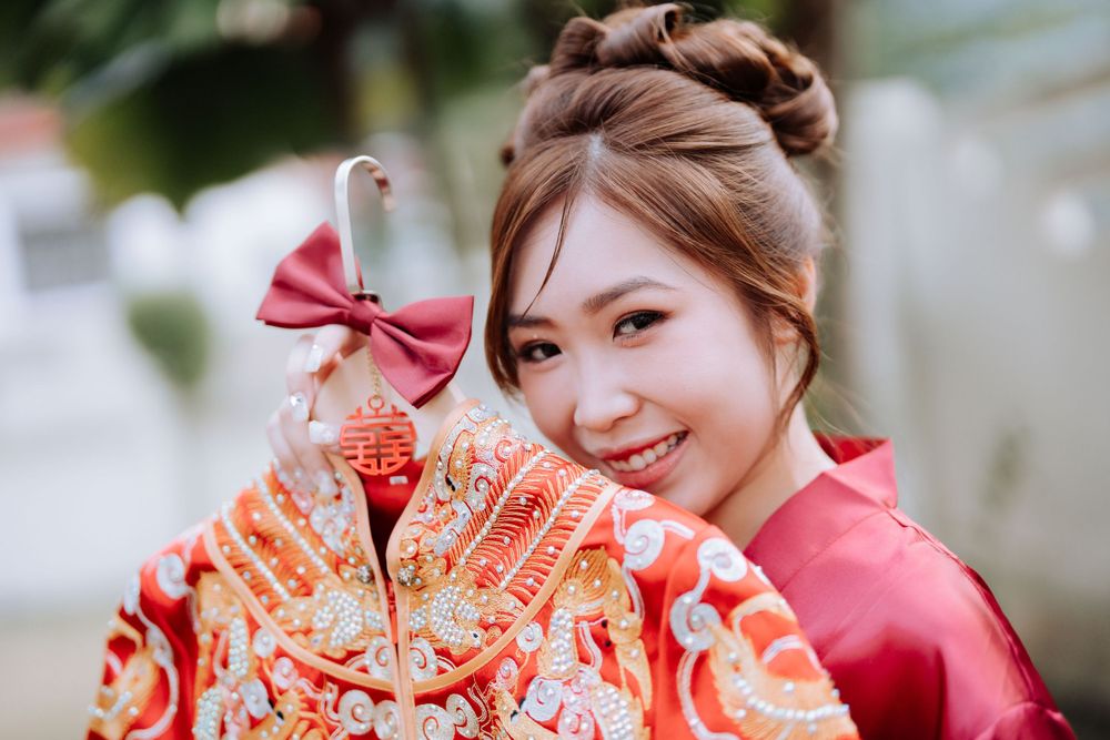 Person in pink robe holding ornate Chinese wedding dress with red bow detail.