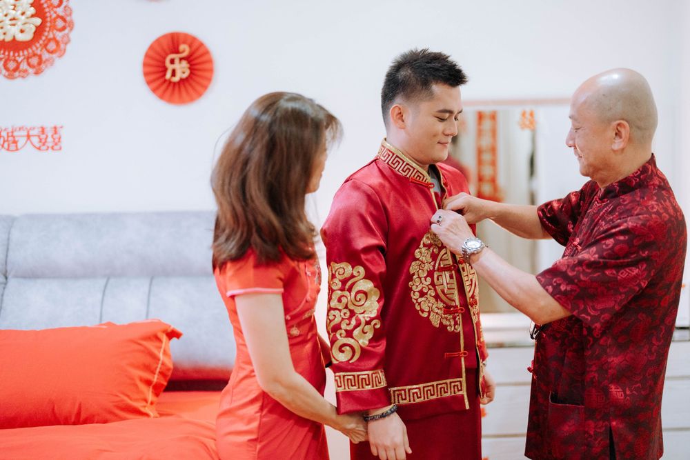 Family members helping dress someone in traditional Chinese wedding attire with gold embroidery.