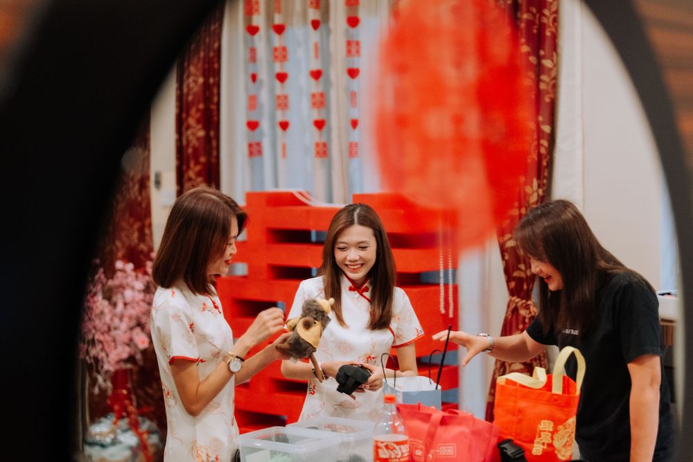 Three people in traditional red Chinese attire sharing a celebratory moment in an indoor setting.