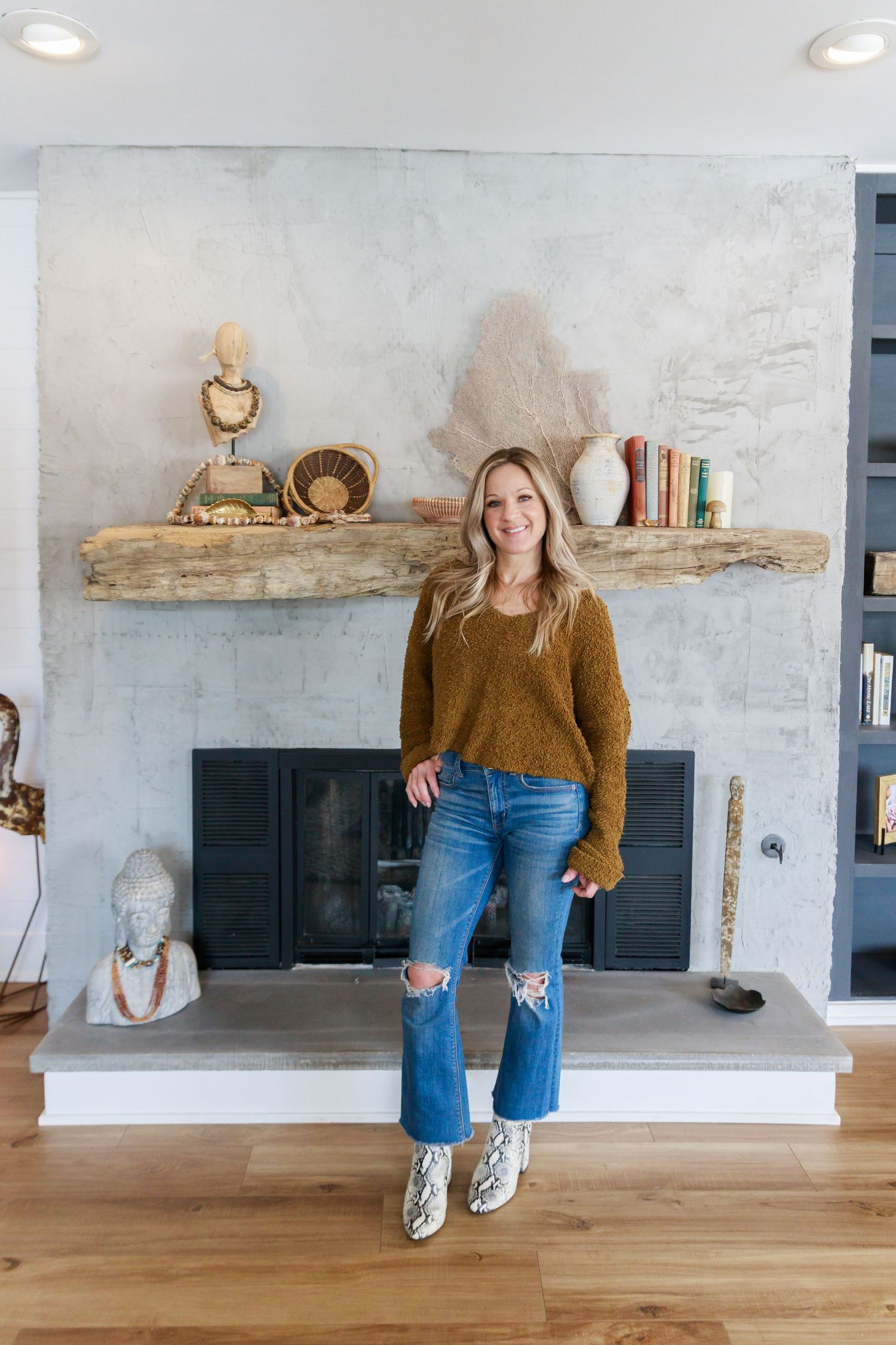 Cozy living room features rustic floating shelves above fireplace, hardwood floors and stylish distressed denim outfit look.