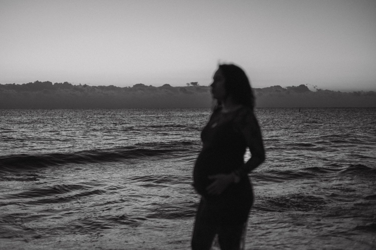 black and white image of a pregnant women posing in front of the ocean