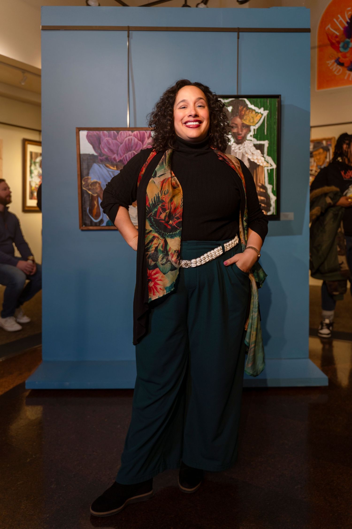 Person in black turtleneck and colorful vest striking confident pose in art gallery space.