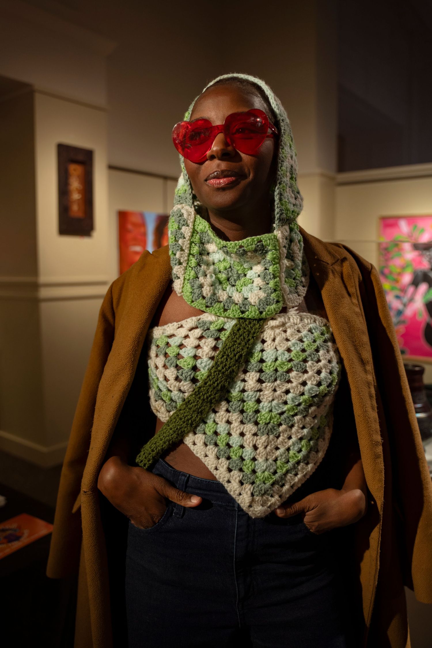 A stylish look featuring a crocheted green and white top, red sunglasses, and brown coat at an art gallery.