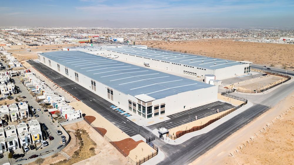 Aerial view of a large modern warehouse facility with a metal roof in an arid industrial area.
