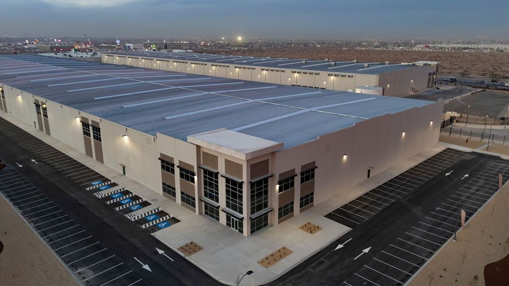 Aerial view of a large modern warehouse facility with solar panels on roof and truck loading docks at dusk.