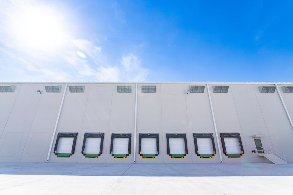 Modern warehouse exterior with multiple loading dock doors under a bright blue sky with sunlight.