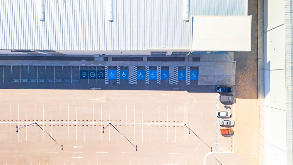 Aerial view of a modern warehouse loading dock with blue doors and parked cars on a sandy lot.