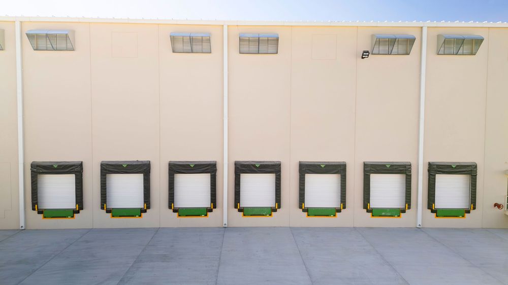 Commercial building exterior with multiple loading dock doors and green bumpers on a beige wall.