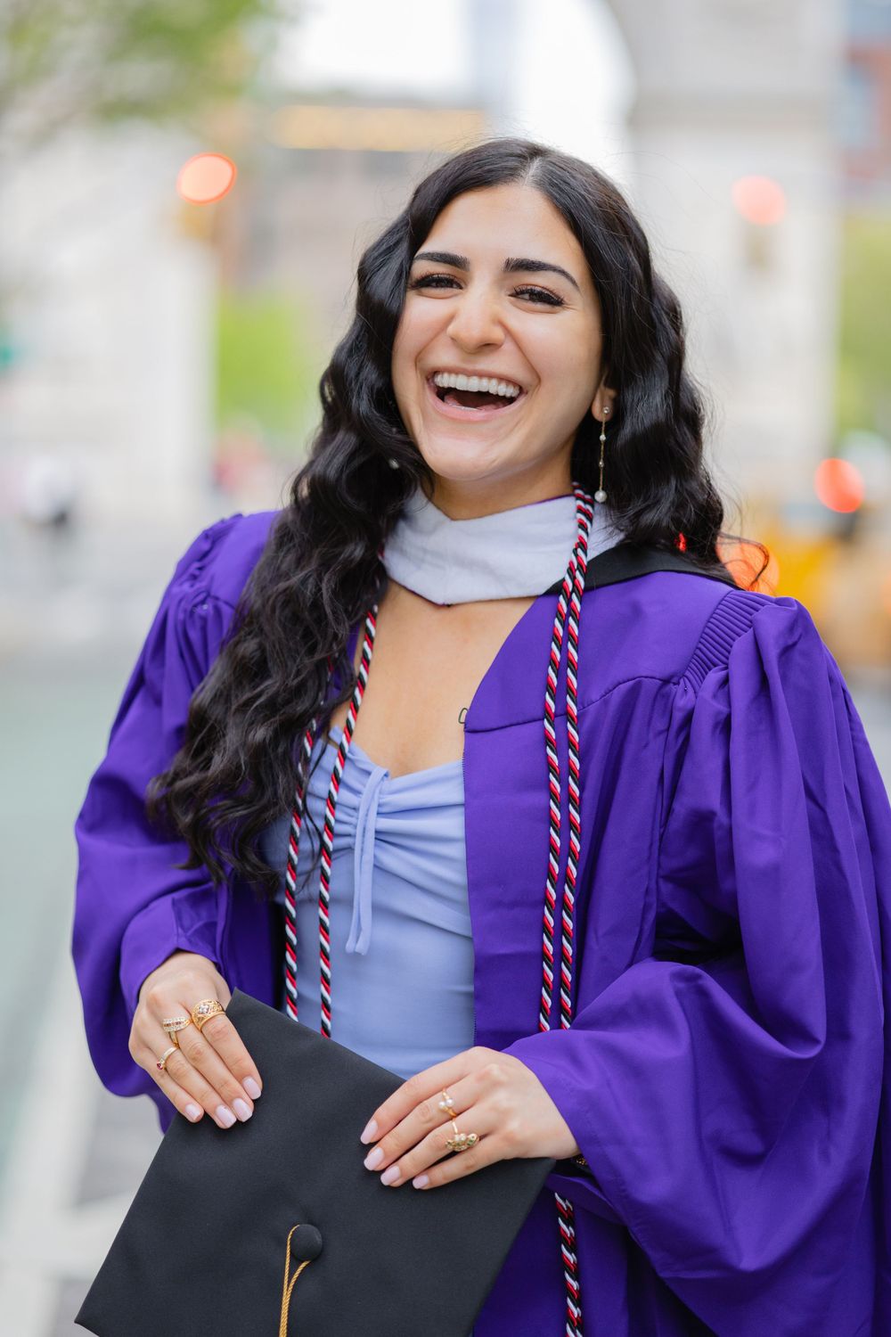 Graduate laughs joyfully while wearing purple commencement regalia and honor cords.