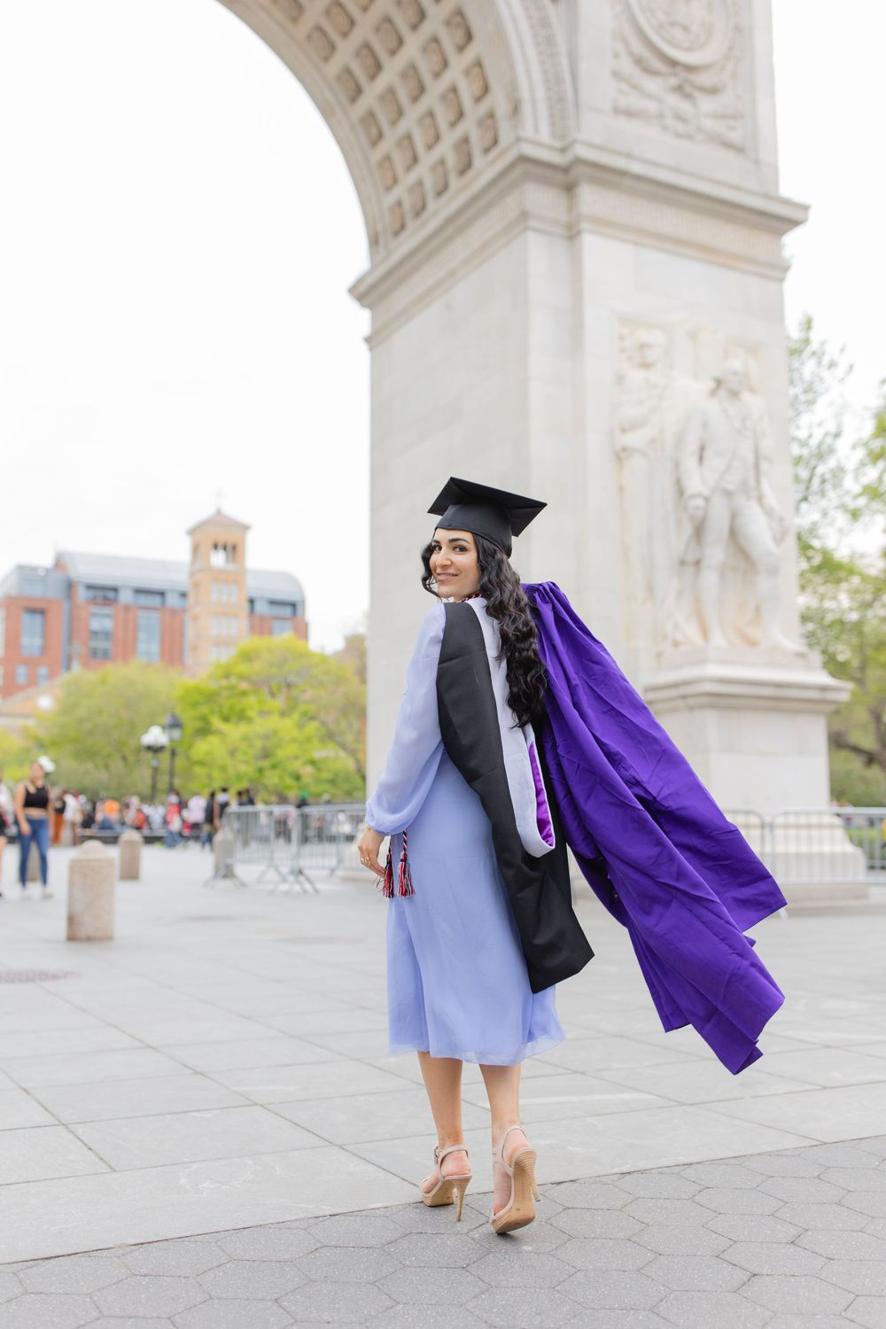 Graduate in flowing purple gown twirls under Washington Square Arch in NYC.
