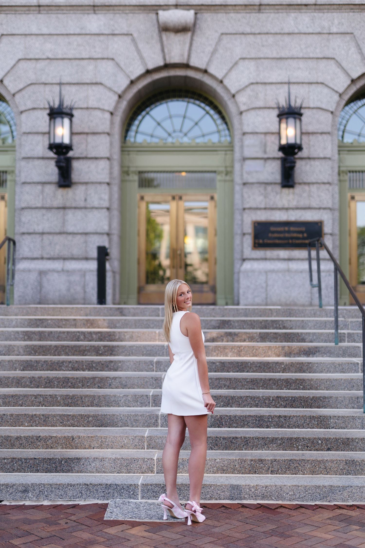 Woman in black top and light jeans sits casually on brick steps in warm outdoor lighting.