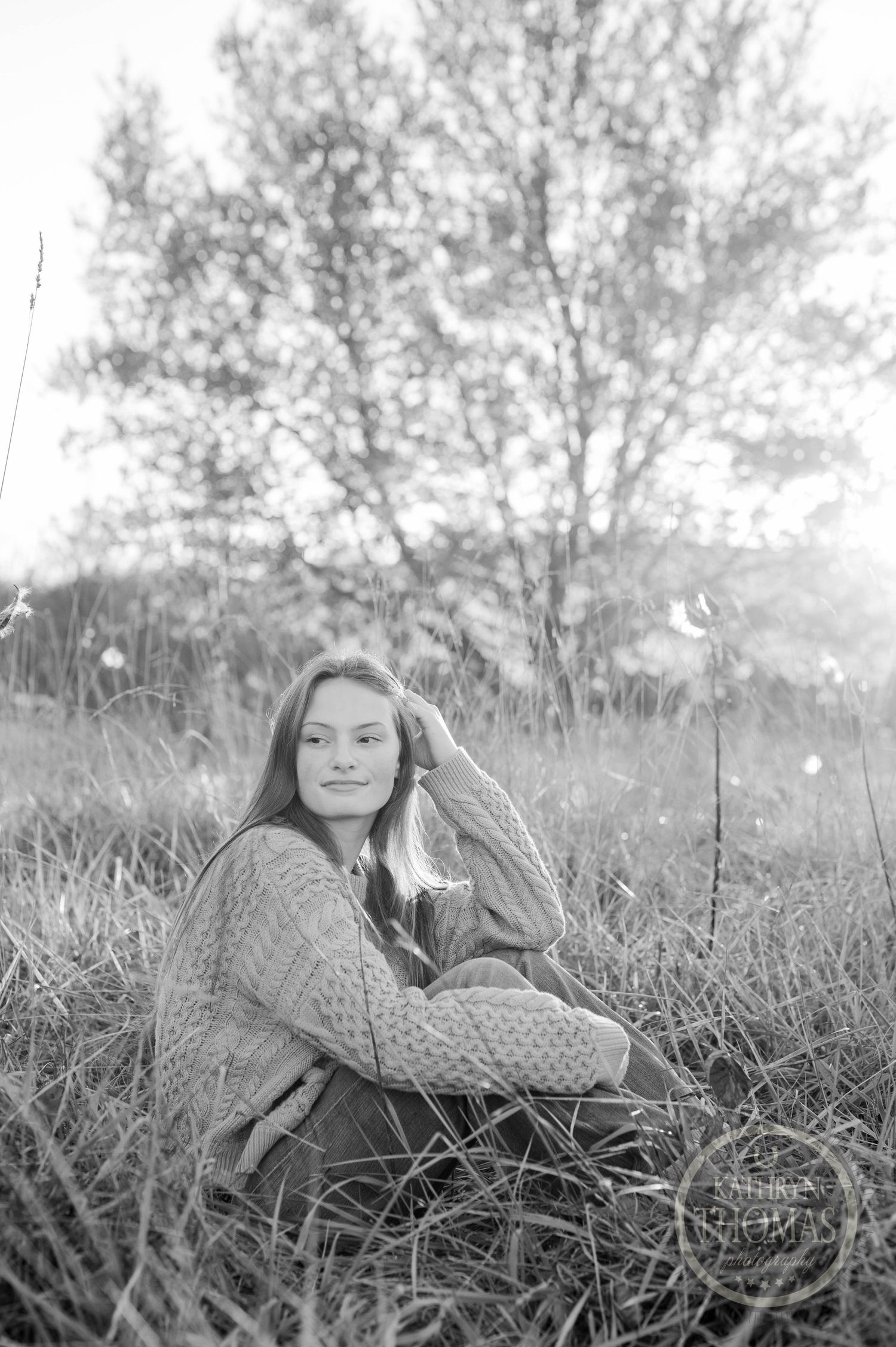 Black and white photo of someone relaxing in a meadow wearing a cable knit sweater.